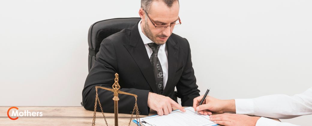 עורך דין לענייני ירושה בחליפה שחורה יושב בשולחנו. בצד שמאל למטה לוגו אתר MOTHERS